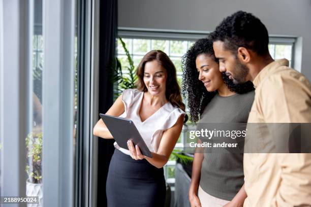 Happy real estate agent showing a couple some pictures using a digital tablet while looking at a house for sale