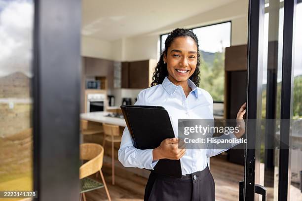 Portrait of an African American real estate agent opening a sliding door at a house for sale and looking at the camera smiling